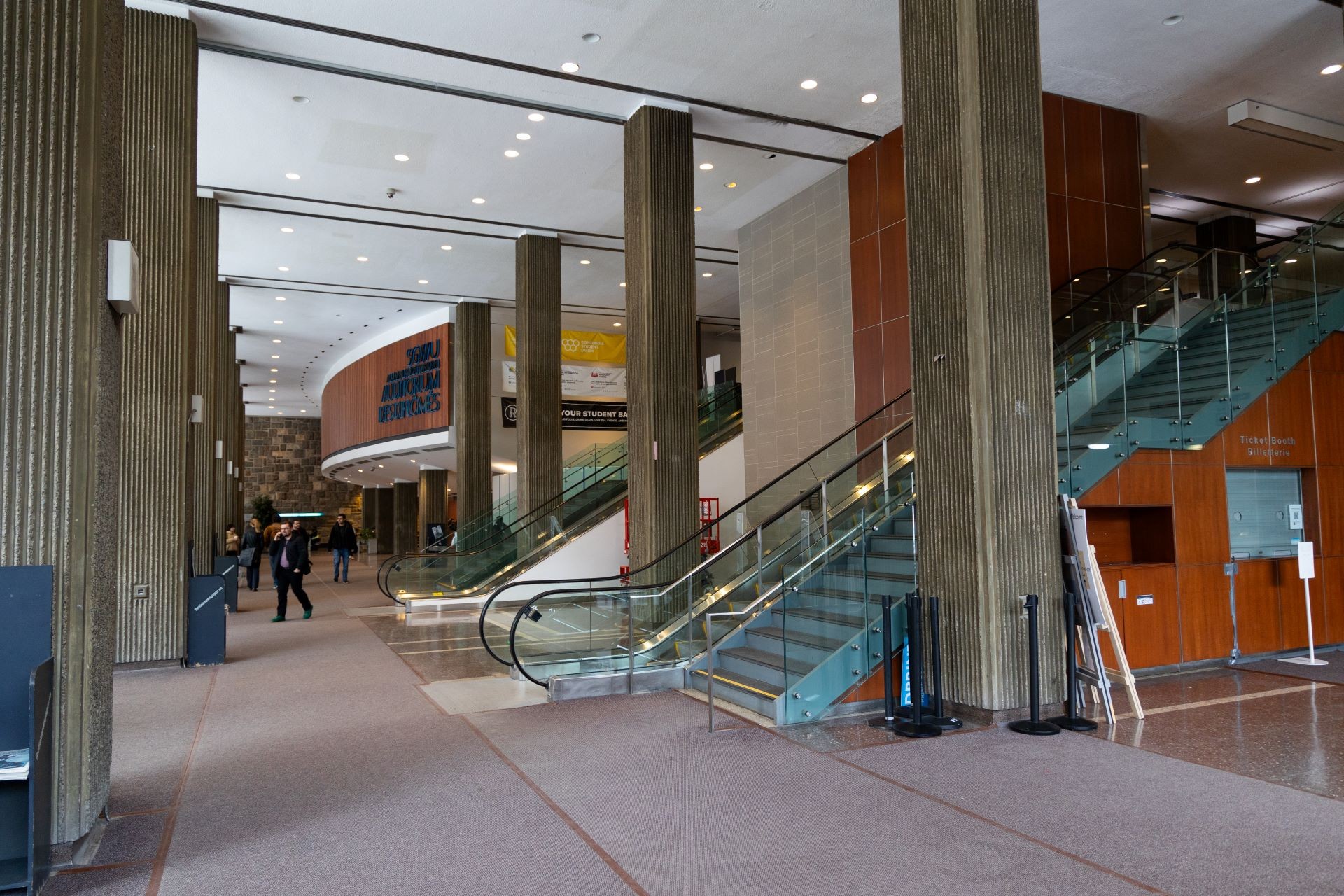 A spacious university hall with modern furnishings and architectural elements, including a staircase and large windows.