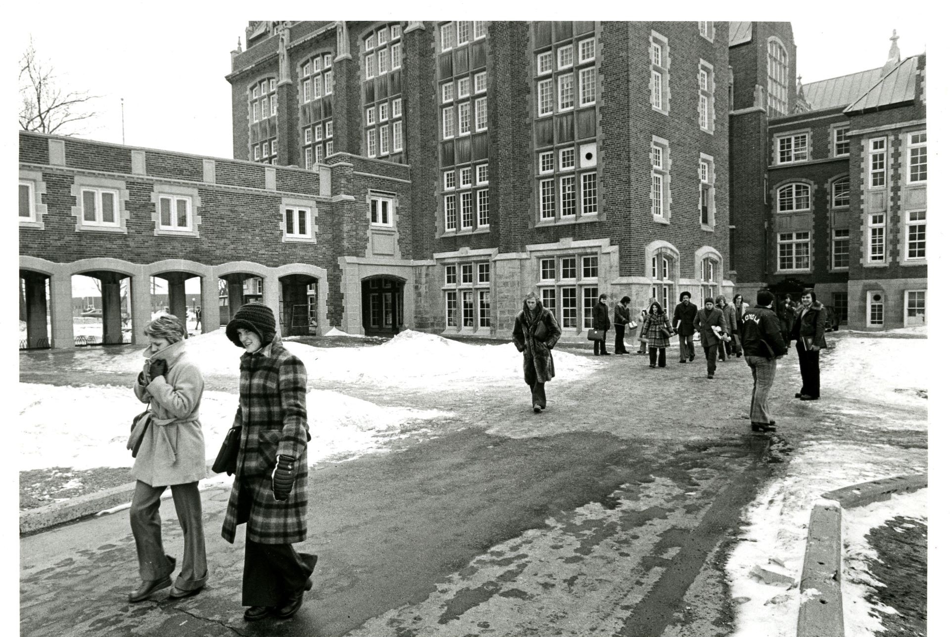 Students walking in winter attire across a snowy campus with traditional architecture in the background.