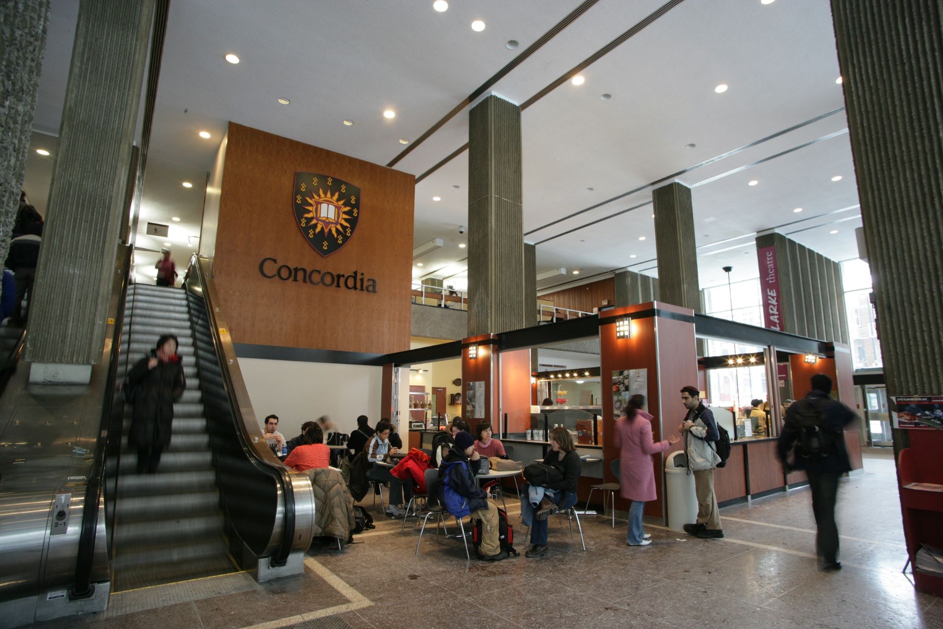 The bustling interior of Concordia University's Hall Building, featuring students and a café area under the university's logo.