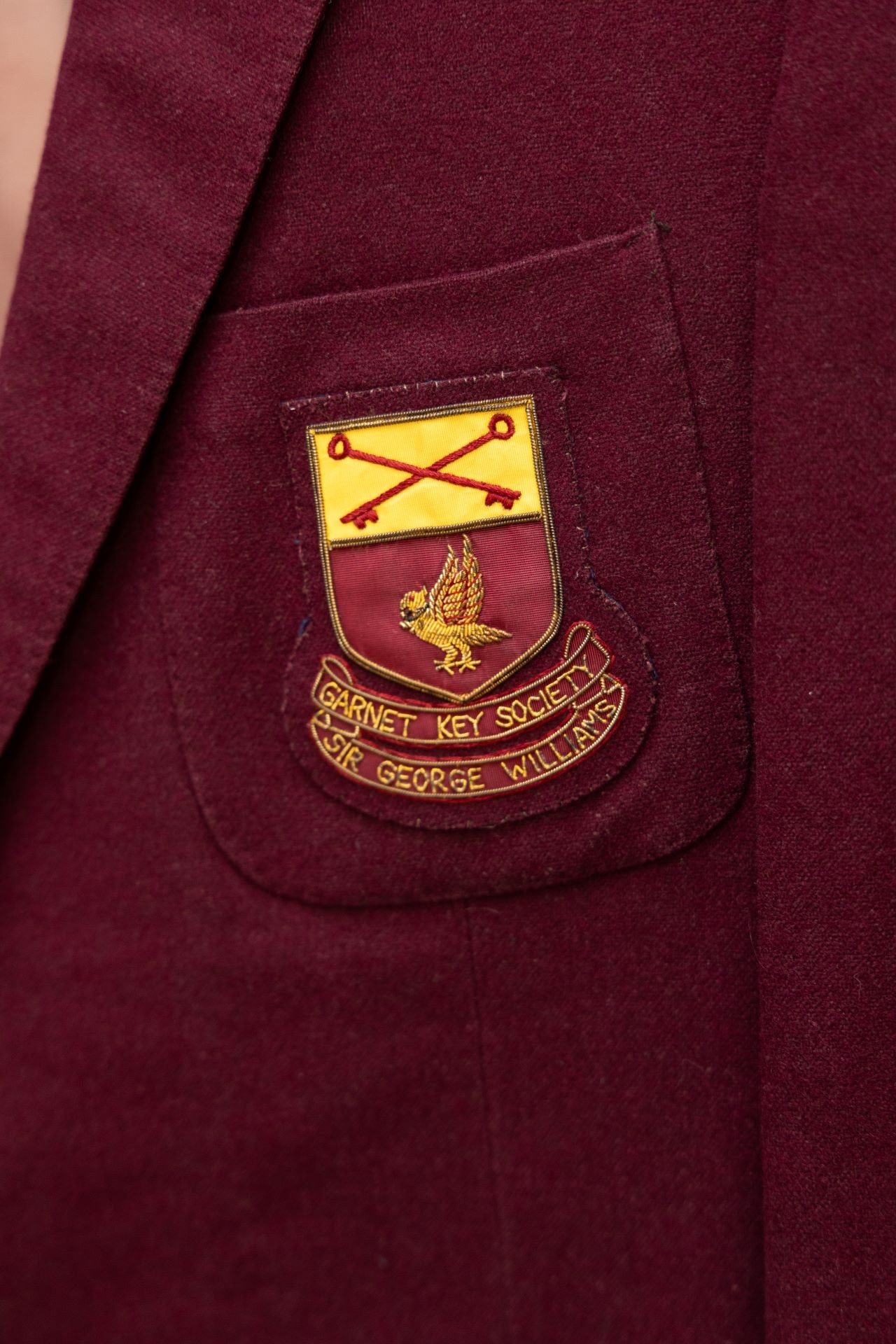 A close-up of a vintage blazer pocket featuring an embroidered patch of the Garnet Key Society from Sir George Williams University.