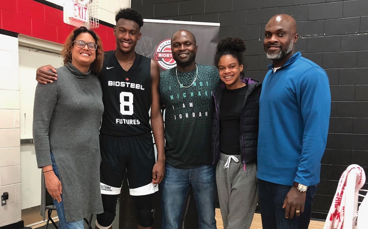 A family group is standing in a gym, with one member wearing a black basketball jersey with "BIOSTEEL 8 FUTURES" on it, and the others smiling and wearing casual clothes.