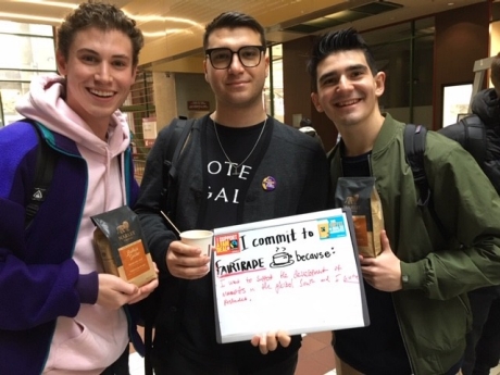 Three students holding a fair trade sign and bags of coffee