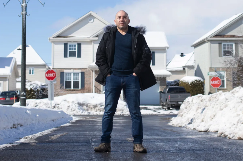A man stands in the middle of a street in a wintry suburban neighbourhood.