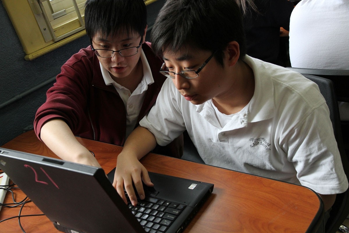 Two teenage boys look at a laptop together