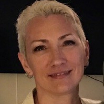 Andrea Tremblay is looking at the camera and smiling. She has short-cropped, bleached hair and is wearing a white jacket.