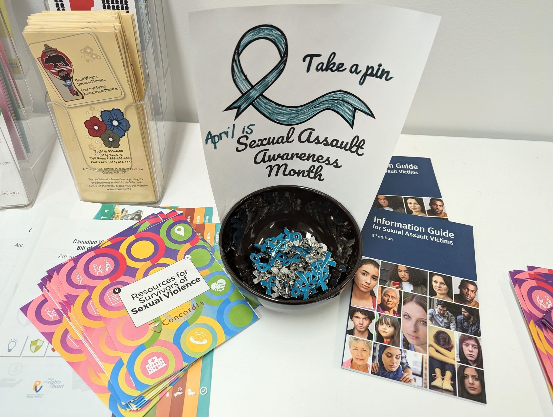 A bowl of teal ribbon pins on a table with information pamphlets about sexual violence