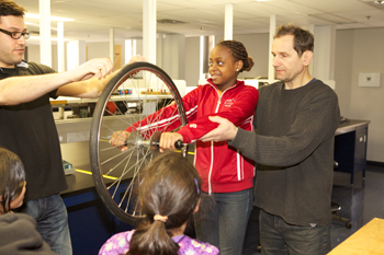 Standing on a rotating platform while holding a spinning bicycle wheel vertically with two hands, the visiting students learned about the physical law of conservation of angular momentum.