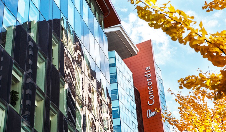 Shot of buildings from below, with the Concordia University logo down the side of one, and autumn leaves on the right of the picture.