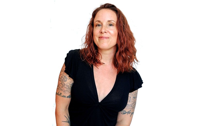 Women with red hair and arm tattoos, dressed in a black shortsleeved t-shirt.
