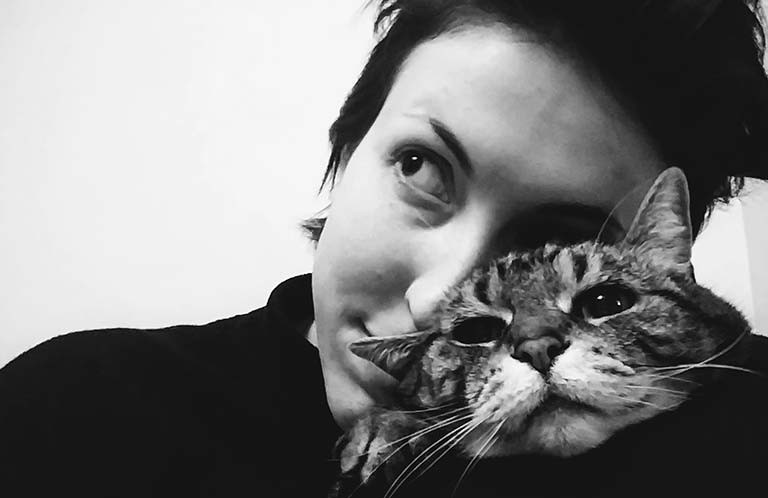 Young woman with short, dark hair cuddling a tabbie cat.