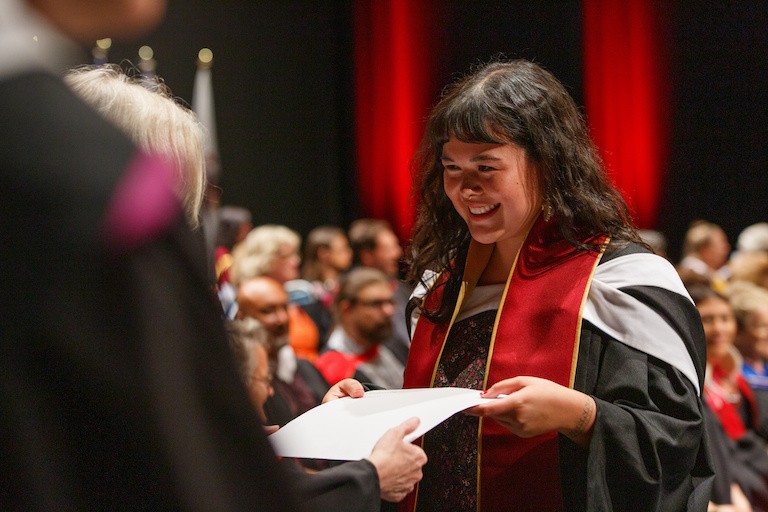 A smiling young woman accepting a diploma, wearing a graduation gown
