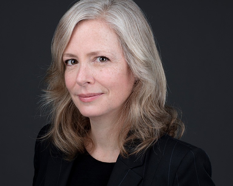 Portrait of woman with mid-shoulder-length hair wearing a black pin-striped blazer and black t-shirt