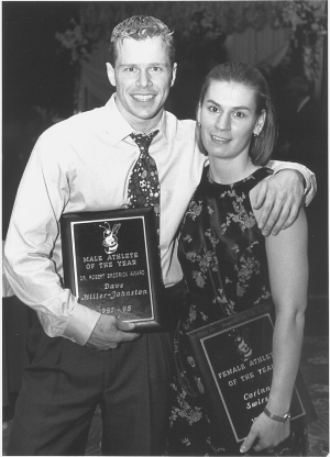 Black and white photo of two people in formal wear holding plaques and smiling