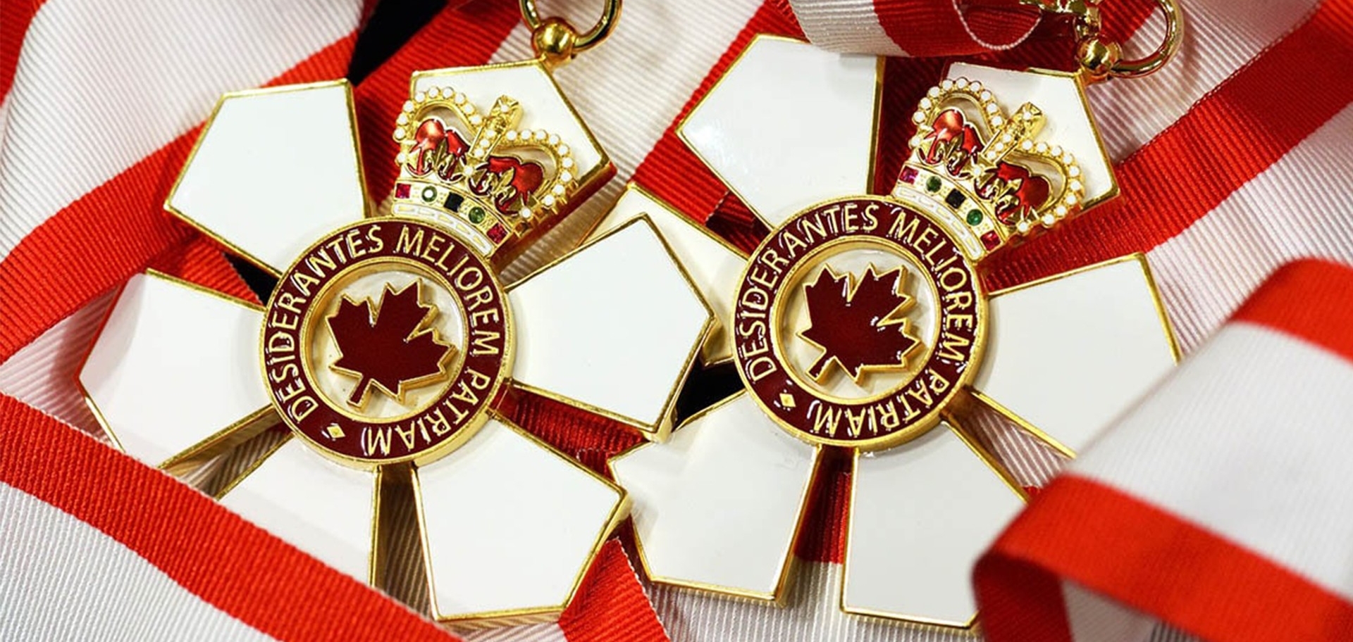 Two six-petaled white medals with maple leaf at the centre and a crown at the top end, attached to red and white ribbons