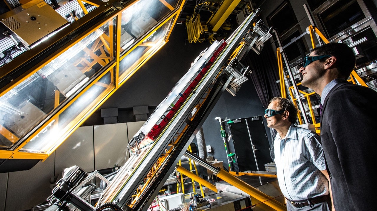 Two scientists observing equipment in a high-tech laboratory setting.