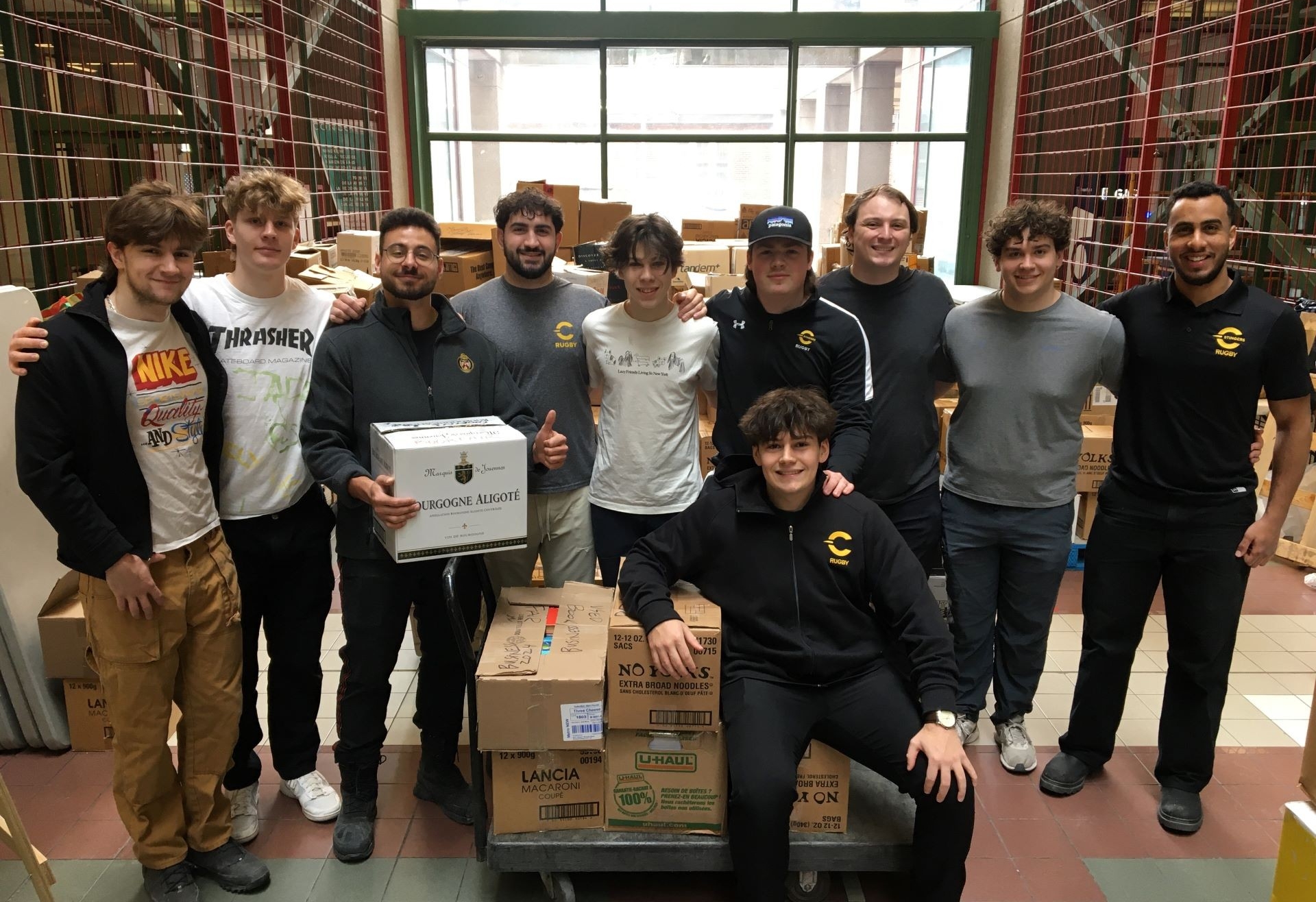 A group of individuals wearing Concordia logo t-shirt's posing with boxes in an indoor setting.