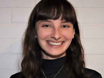 Jeune femme souriante aux longs cheveux noirs, portant un col roulé noir.