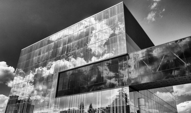 Image in black and white of a building made of glass, with a glass tunnel stretching from the building to beyond the edge of the photo.