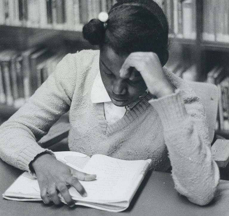 Girl reading at a table in front of a bookshelf, probably at the library in the Negro Community Centre. | Photo: Graeme Clyke