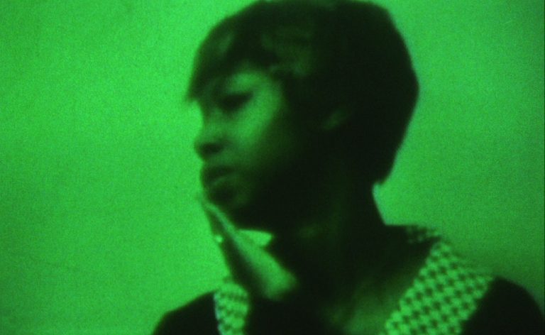 A black woman with short hair, her hand to her face, with a green-wash tint to the image.
