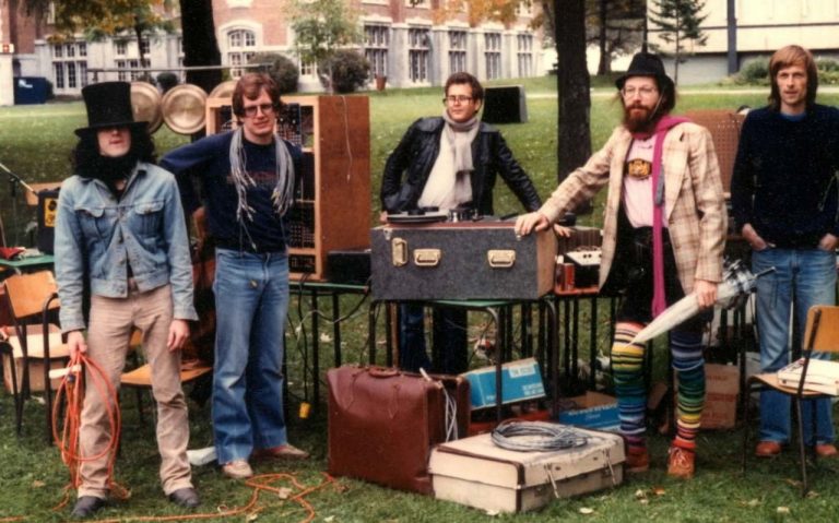 An archive photo c. 1982 of a group of musicians on a university lawn, with all their instruments