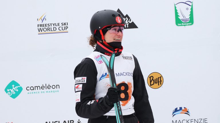Young woman in a ski competition outfit, a helmet, goggles and holding a pair of skis.