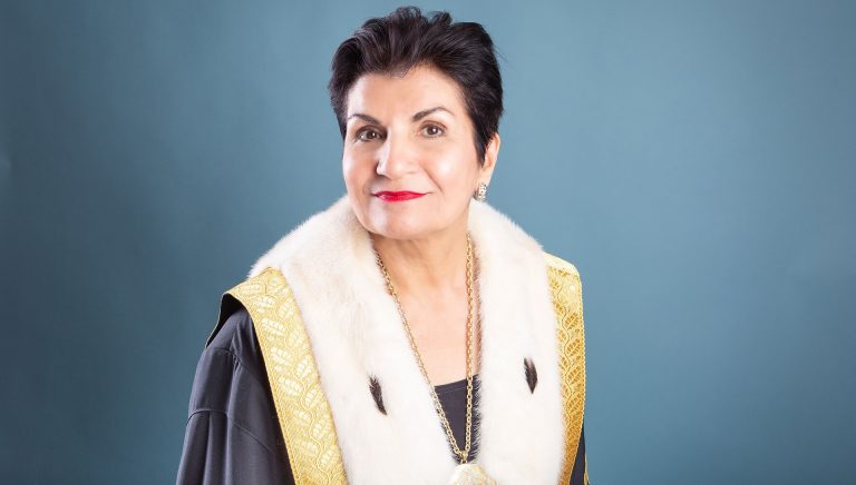 Smiling woman with short, dark hair wearing the ceremonial robes of a university co-chancellor