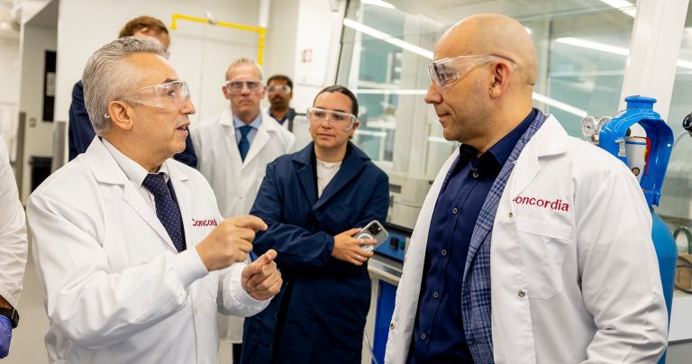 Men and women in a university lab, wearing lab coats and safety glasses