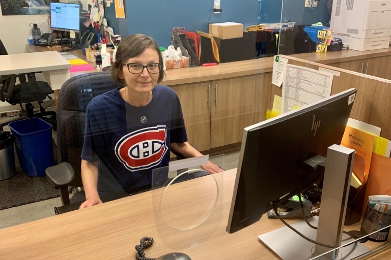 Une femme portant un t-shirt des Canadiens de Montréal est assise à un bureau derrière une vitre en plexiglas.