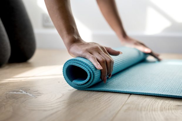 A woman rolls up a yoga mat on a hardwood floor.