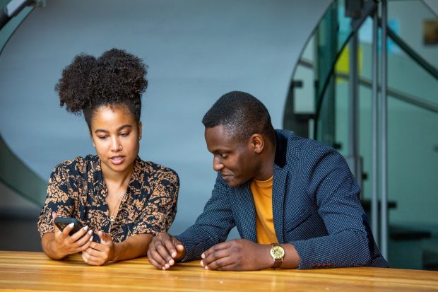 Two people looking at a smartphone together at a table.