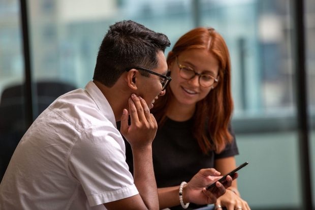 Two individuals engaged in a cheerful conversation, with one holding a smartphone.