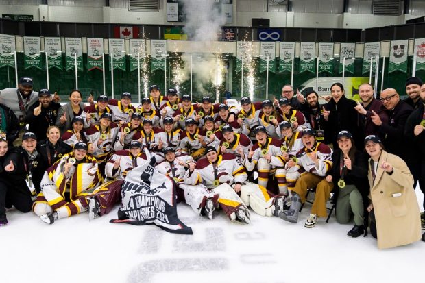 A women's sports hockey team on the ice, gathered together for a group photo, celebrating a win at Nationals.