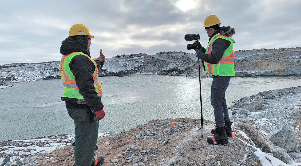 Two people wearing bright vests use measuring equipment in the far north