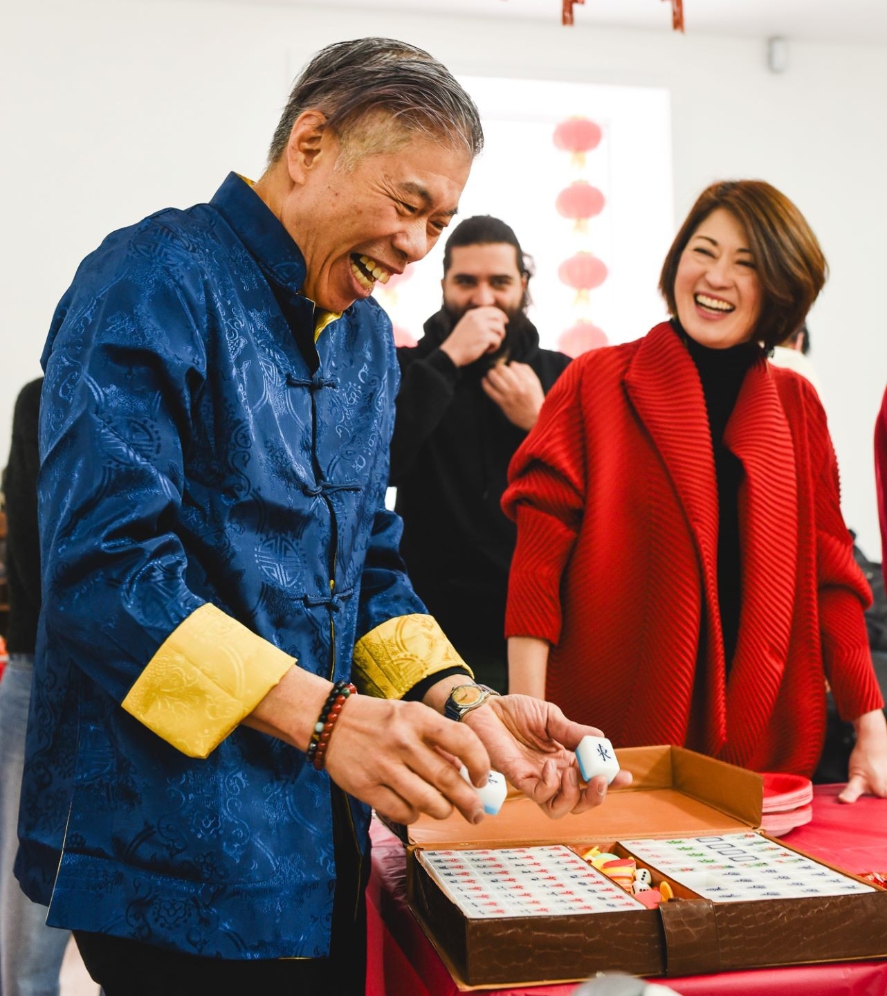 Two individuals laughing and standing over a box of Mahjong tiles