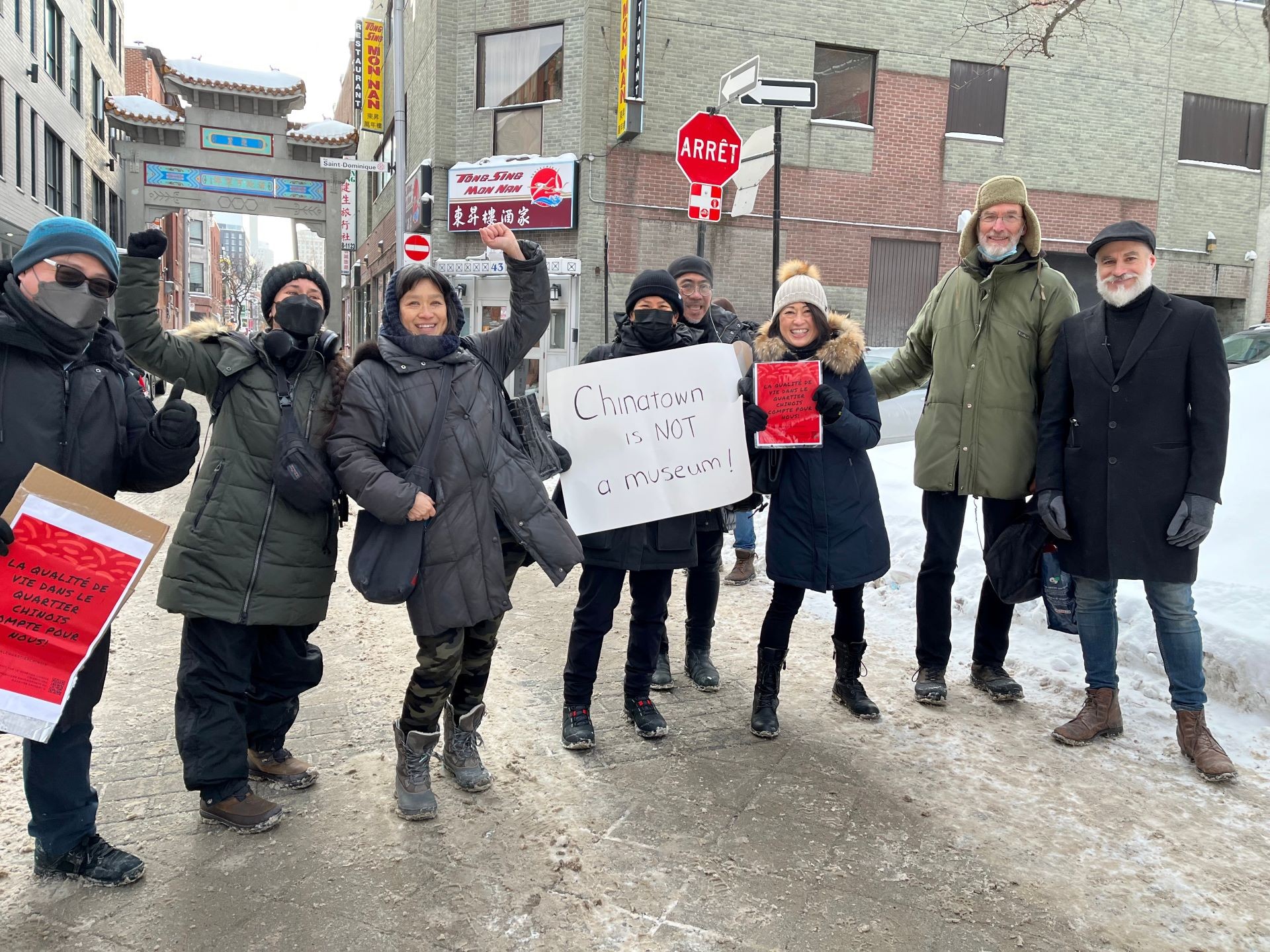 A group of people standing outside in winter, holding a sign that reads "Chinatown is not a museum"