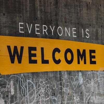 A grey concrete wall with the words "Everyone is Welcome" painted above graffiti