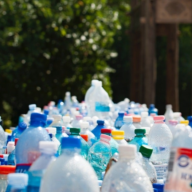 A long line of plastic bottles of different shapes and sizes with trees in the background