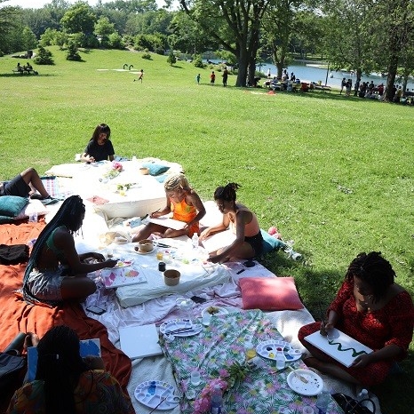 Black women seated and painting in a park