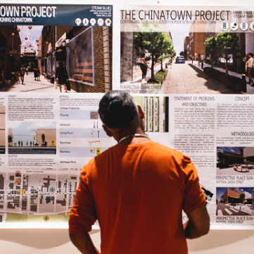 A photograph of an individual standing in front of Chinatown history posters.