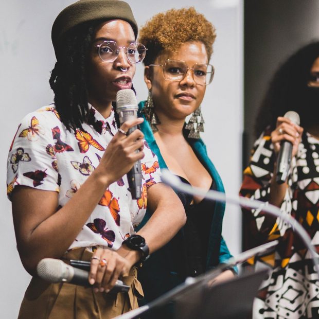 A photograph of two members of the Harambec team speaking into a microphone at an event