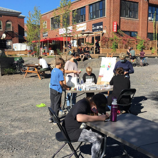 A photograph of people doing arts activities outside of a building, in a parking lot.