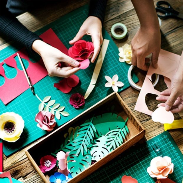 A photograph taken from above of hands doing an arts project on a table.