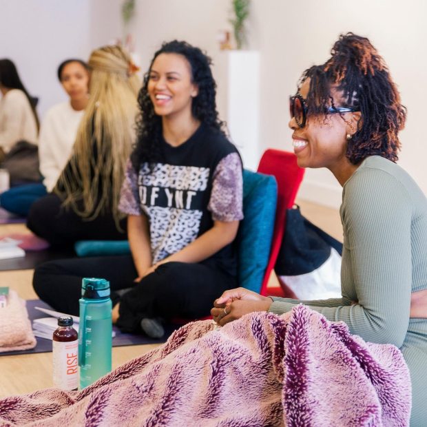 A photograph of two individuals laughing to an unseen speaker while sitting on yoga mats.