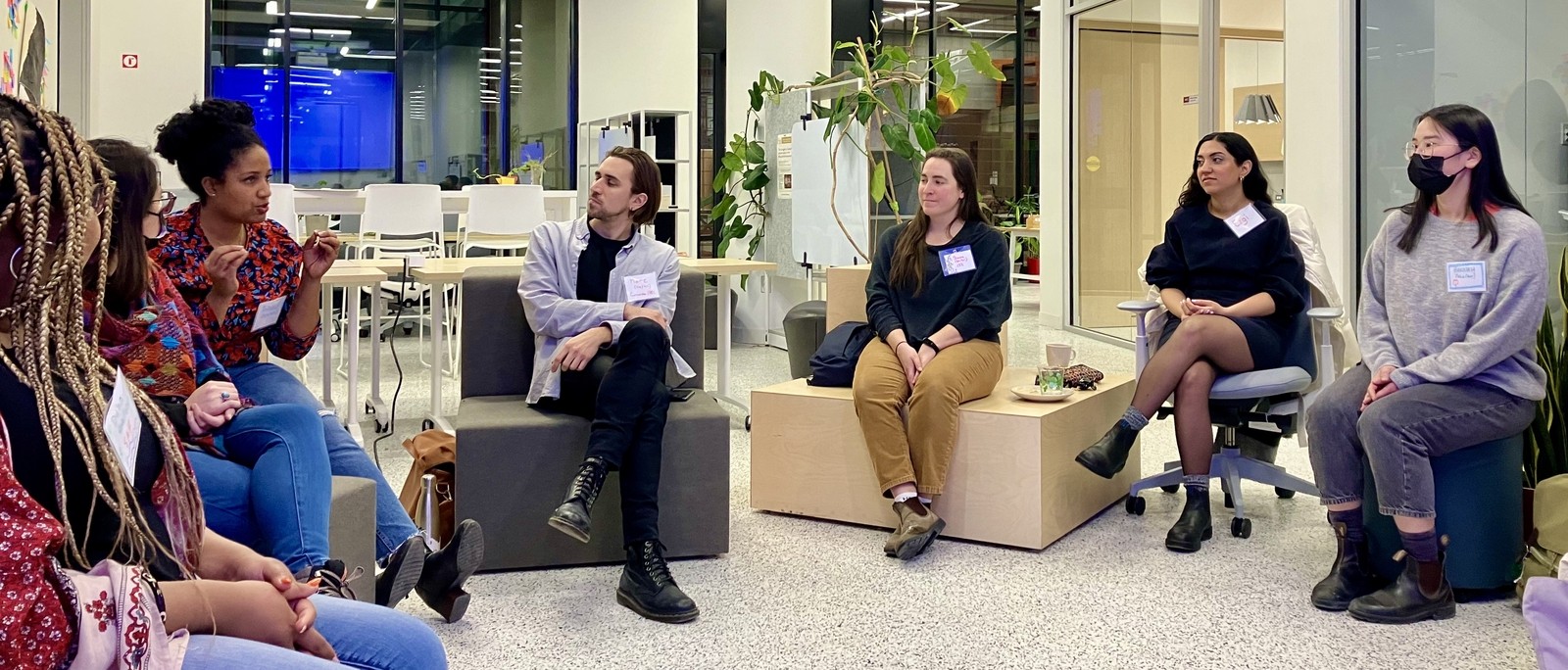 Photograph of a group of people, some masked, sitting in a circle discussion
