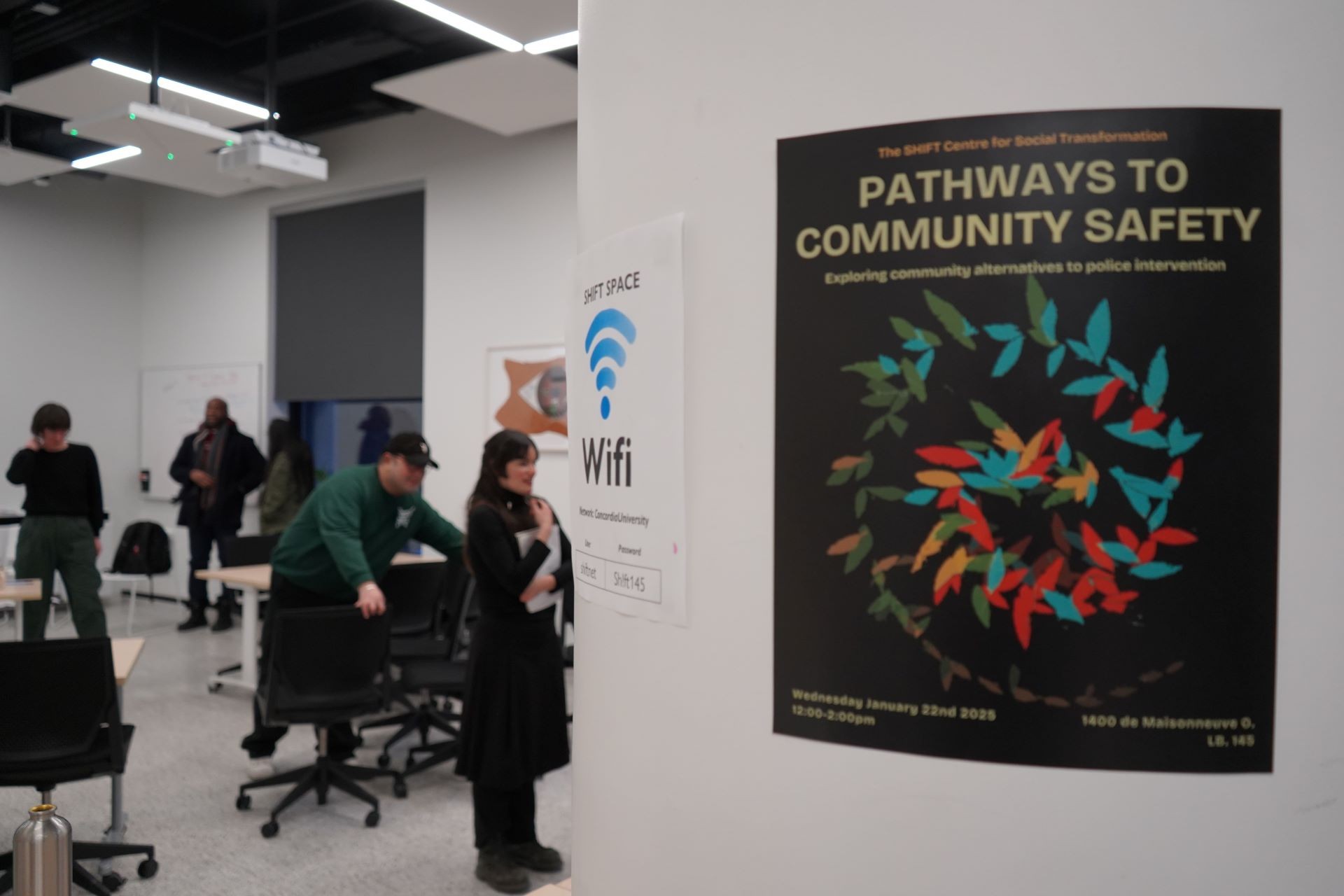 In the foreground, a poster of the Pathways to Community Safety event. People standing in the background.