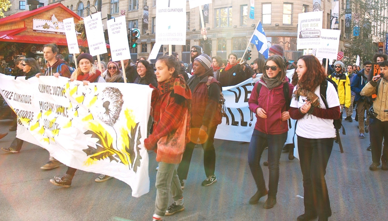 Hundreds of people marching on the streets of Montreal holding climate justice banners, signs, and Quebec flags.
