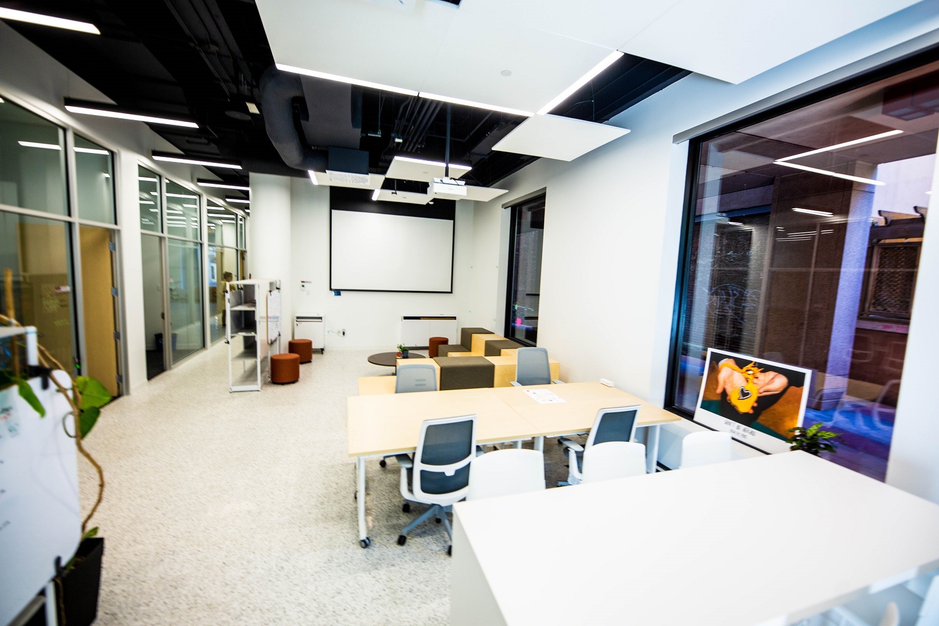 An open area with two tables and office chairs, a screen and projector, and a couch area with coffee table