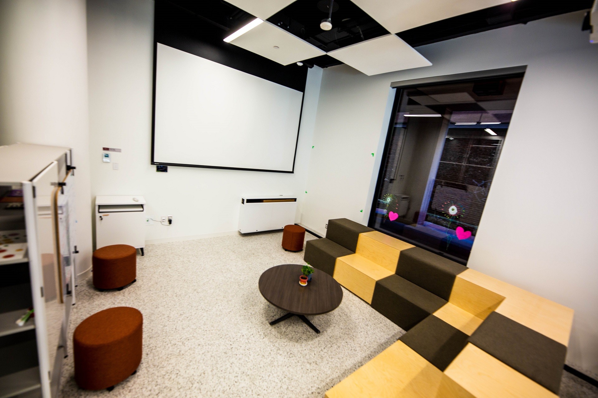 An L-shaped couch, stools and table in front of a screen on the wall