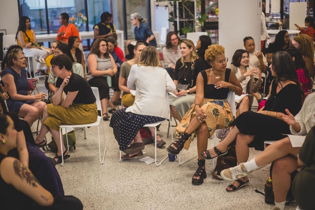 A large group of people sitting in the open space and conversing.